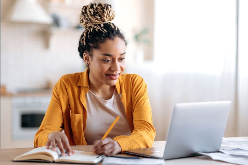Young woman in orange shirt with laptop studying English online